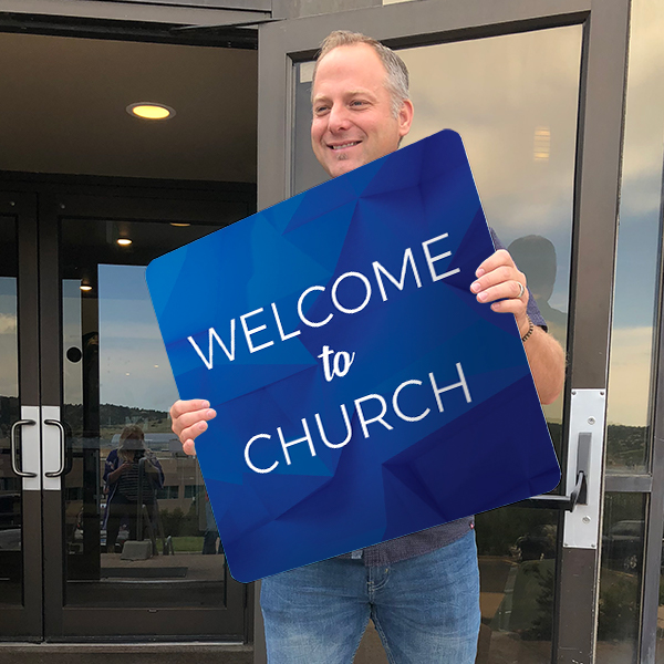 a man holding a blue sign that says Welcome to Church